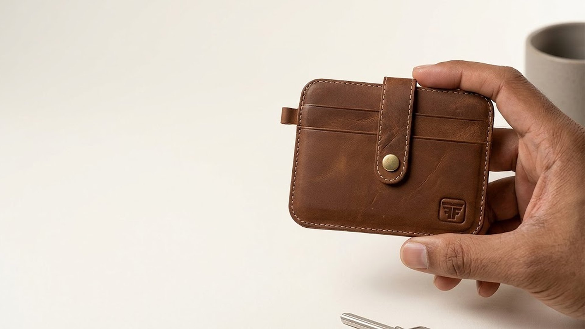 A hand holding the Fashion Freak slim strap leather card holder in Hunter Brown