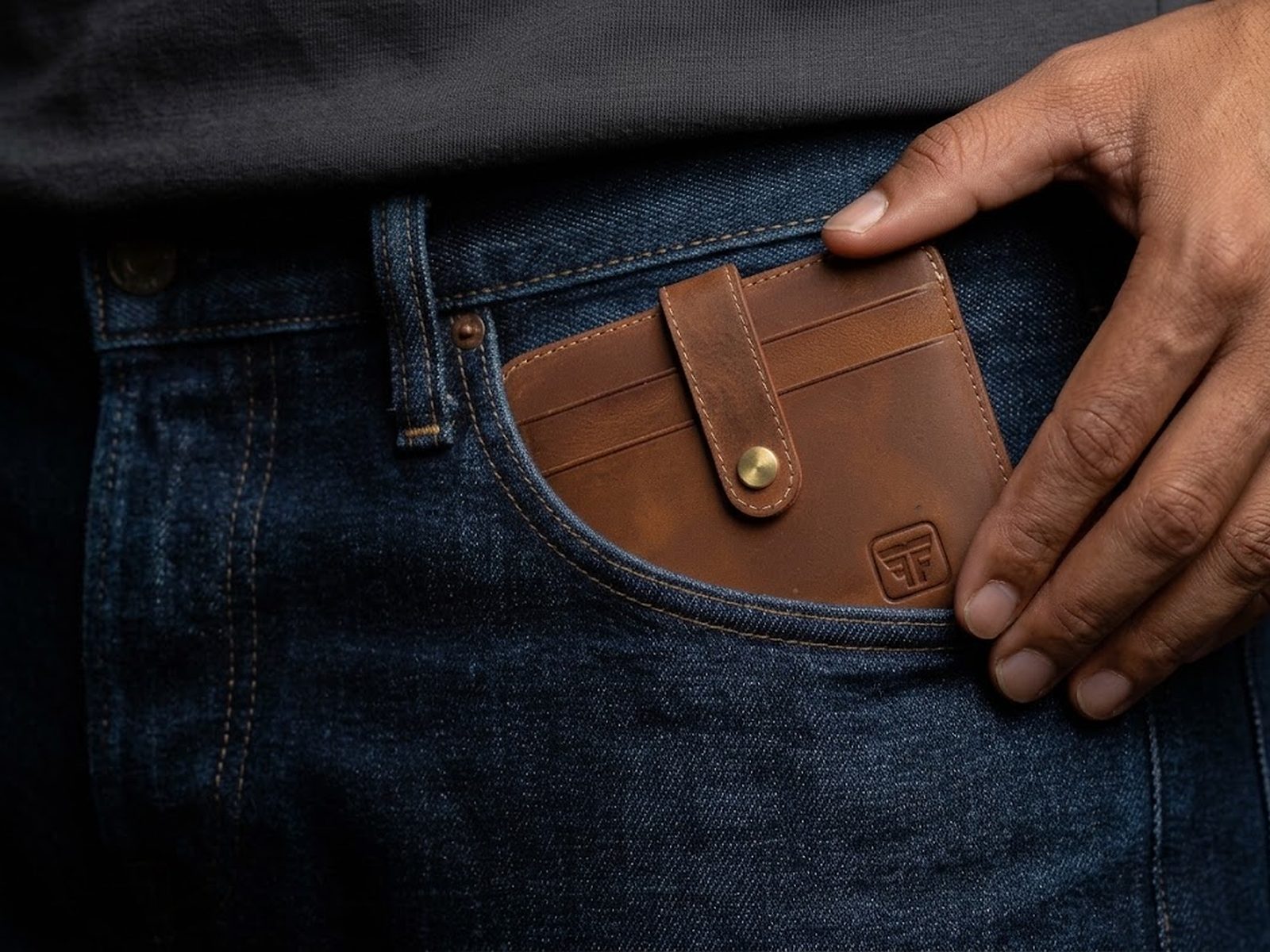 A hand sliding the Fashion Freak leather card holder flat into the front pocket of dark indigo jeans